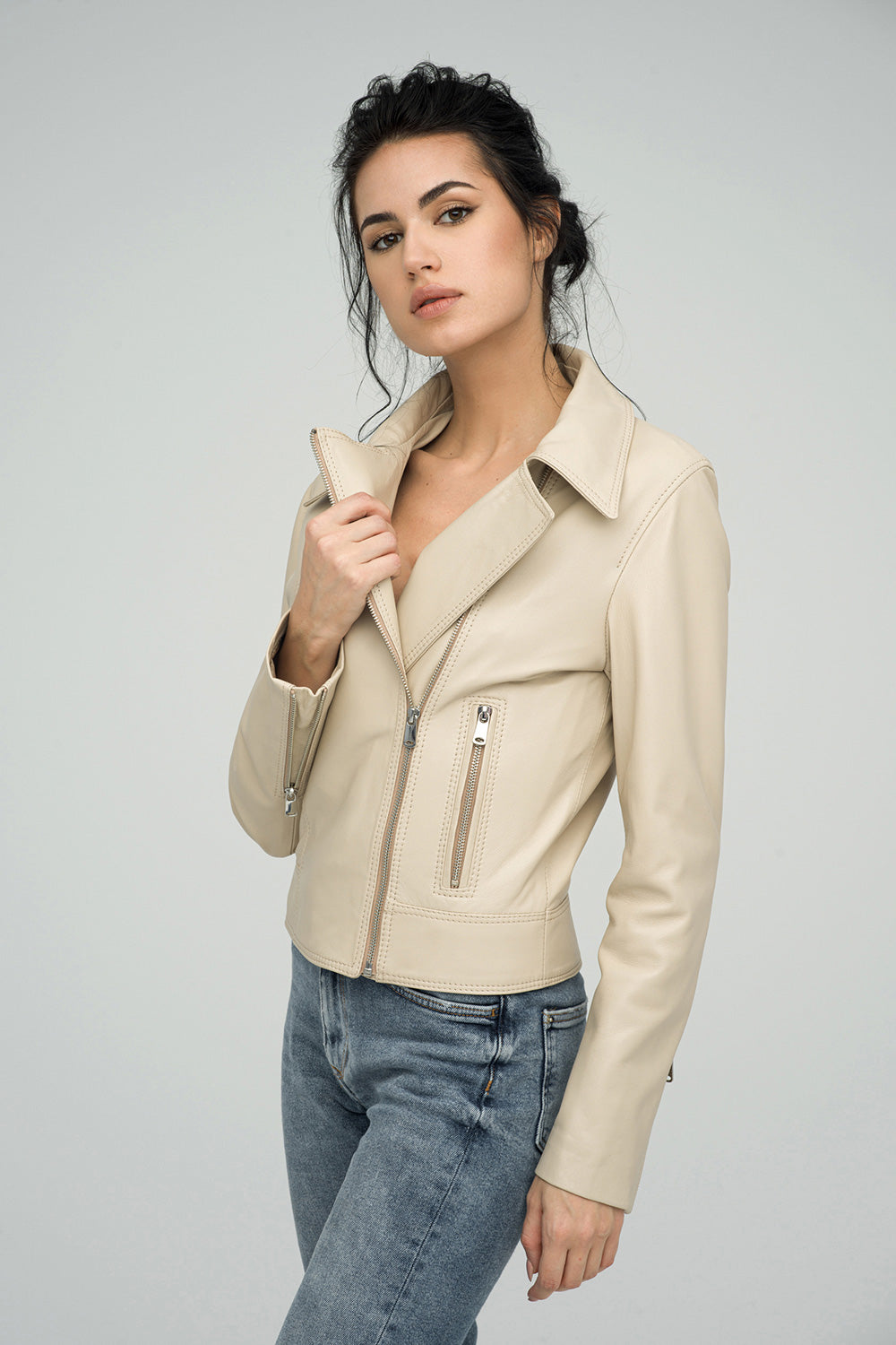 Woman wearing a beige leather jacket and blue jeans on a light gray background