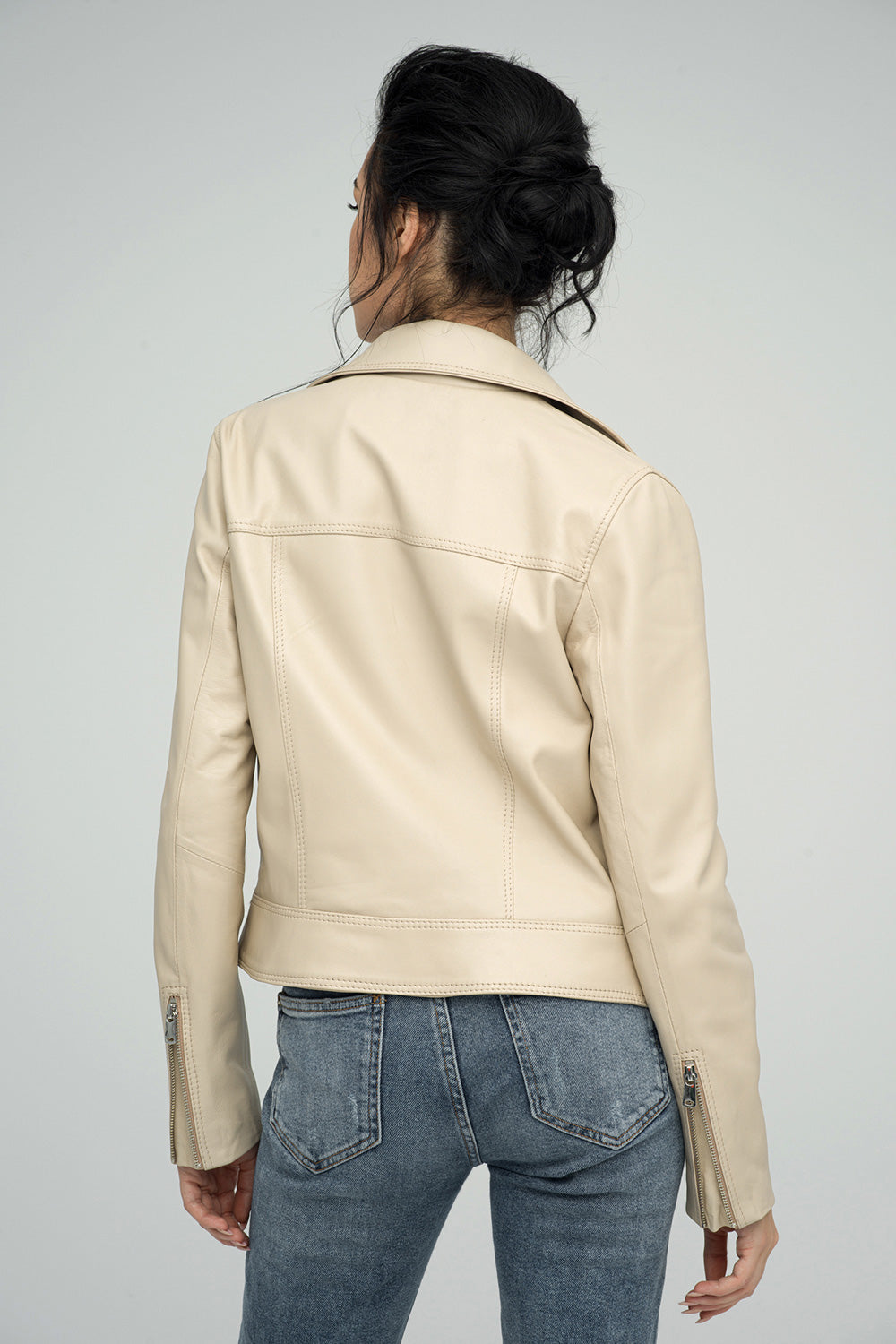 Person wearing a beige leather jacket and blue jeans on a gray background