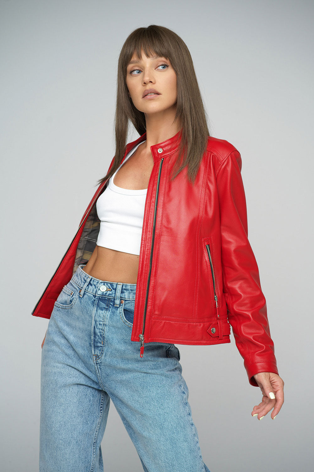 Woman wearing a red leather jacket and blue jeans on a gray background