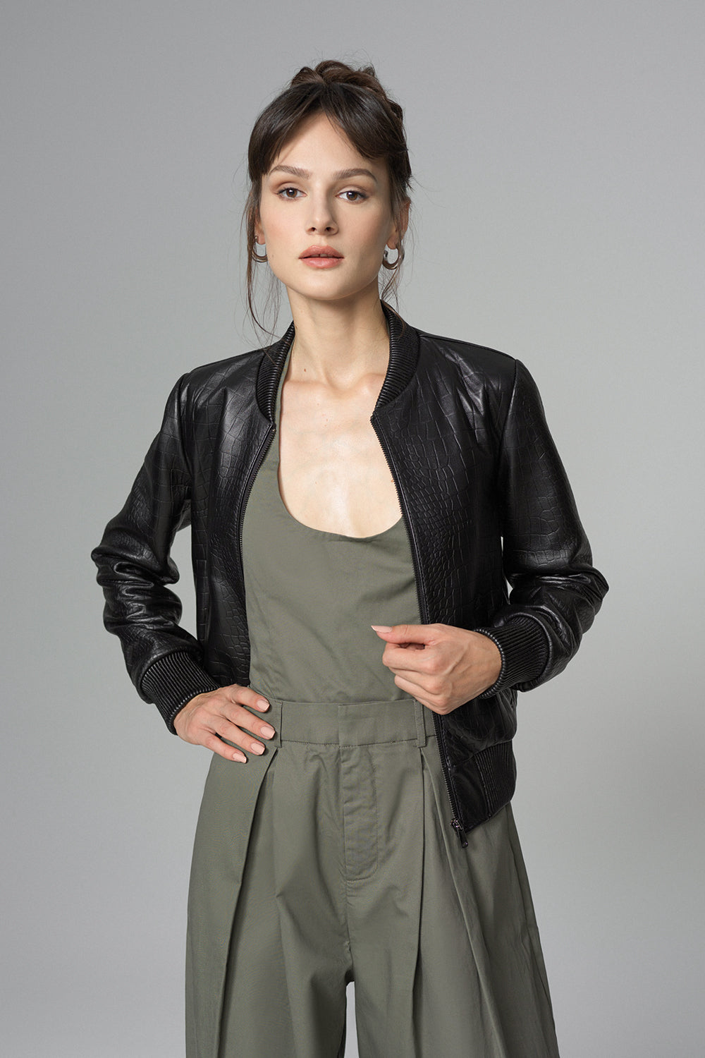 Woman wearing a black leather jacket over a green jumpsuit on a gray background