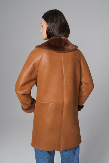 Person wearing a brown leather coat with fur collar on a gray background