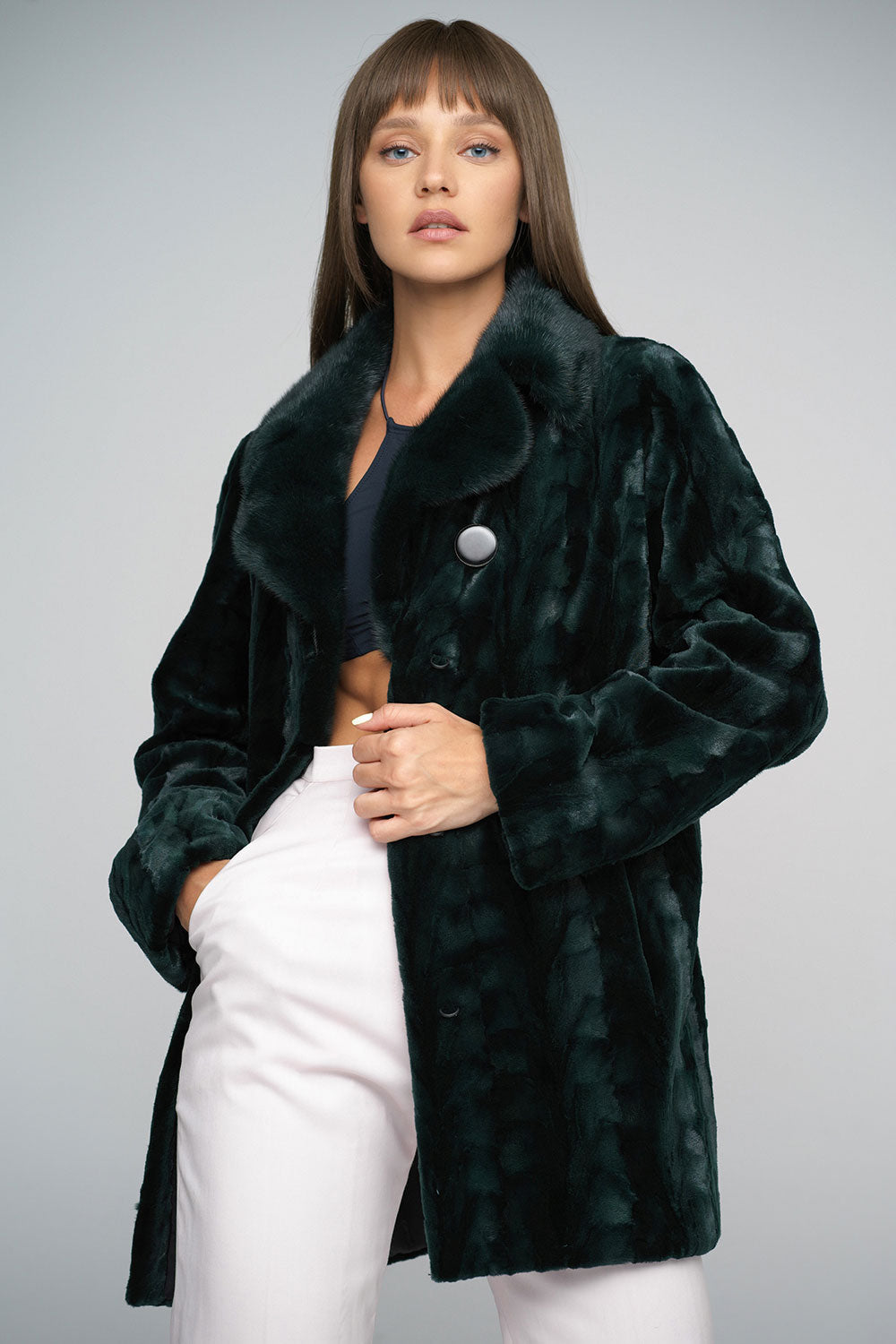 Woman wearing a dark green fur coat against a gray background