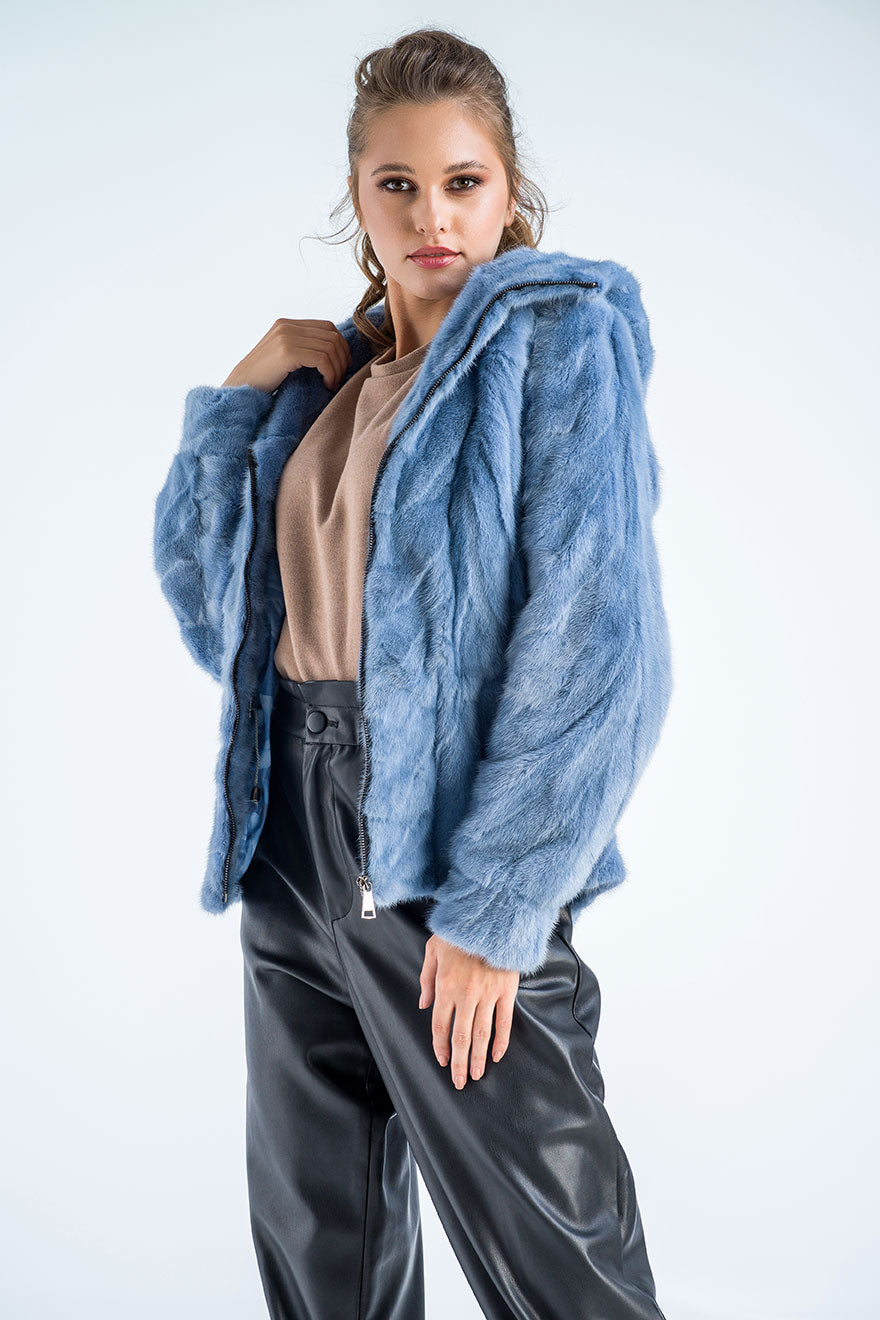 Woman wearing a blue fur coat over a beige top and black pants on a white background