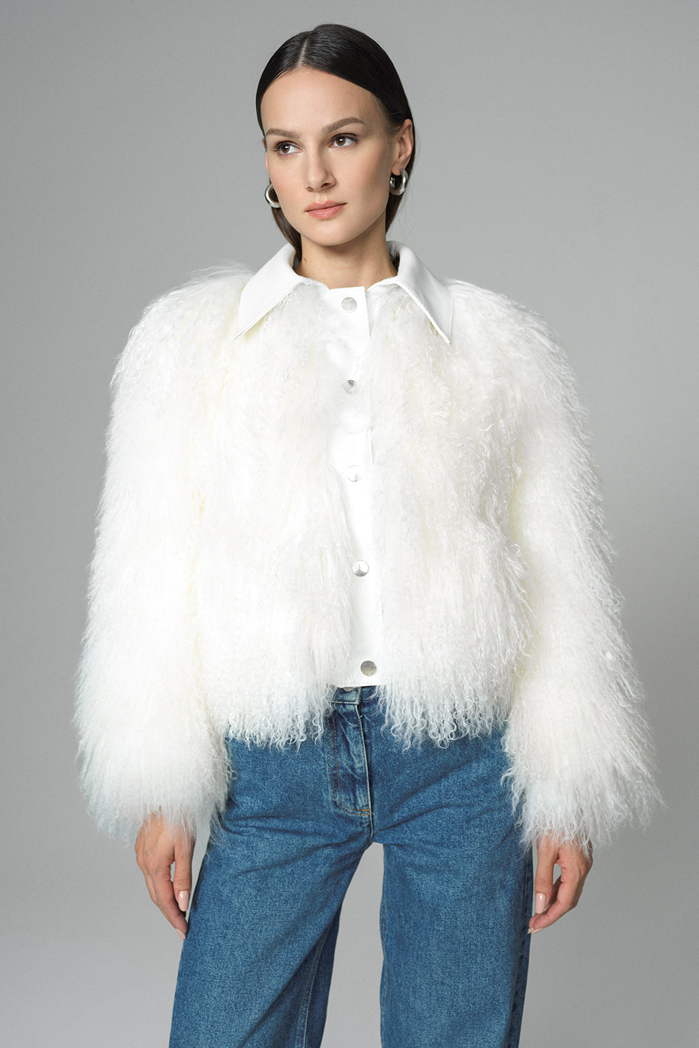 Person wearing a white fur jacket and blue jeans on a gray background
