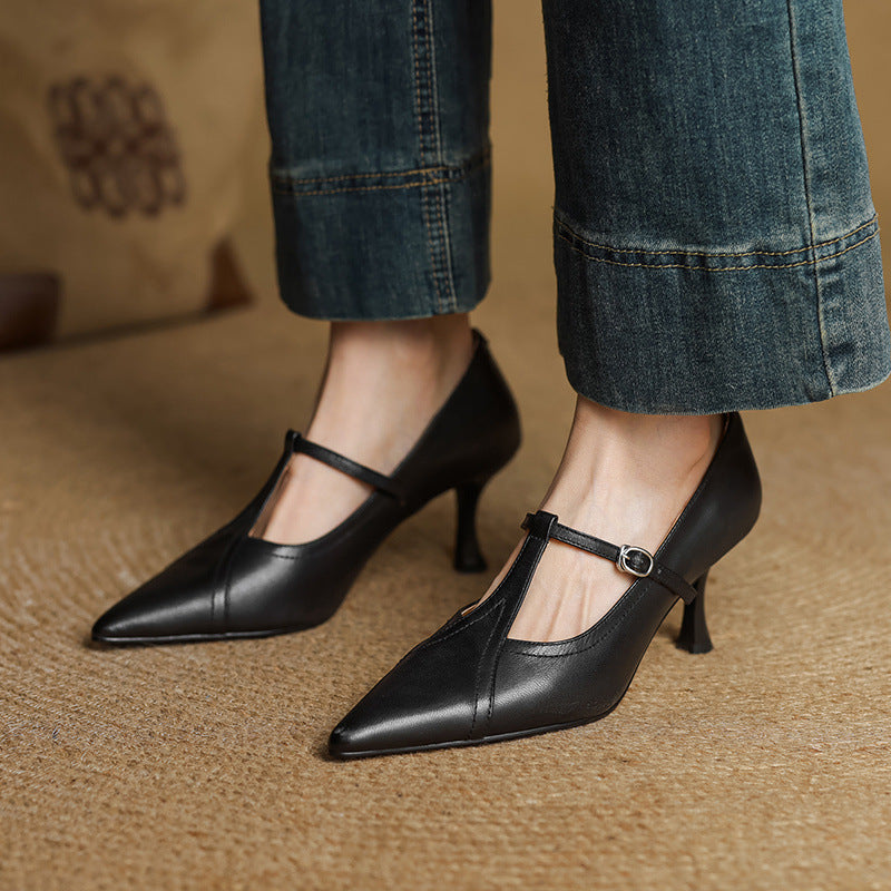 Black high-heeled shoes with thin straps worn with blue jeans on a textured surface.