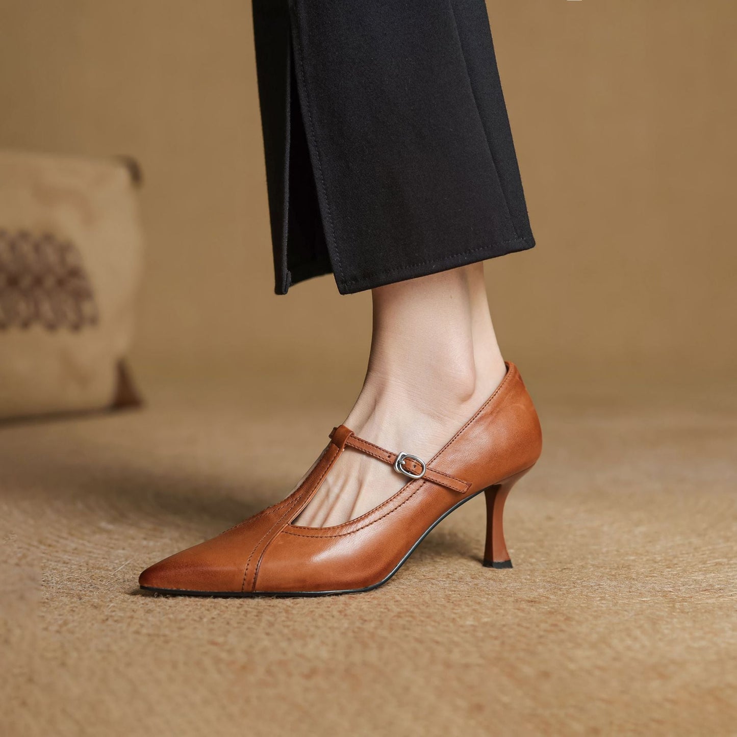 Brown high-heeled shoe worn with black pants on a beige background