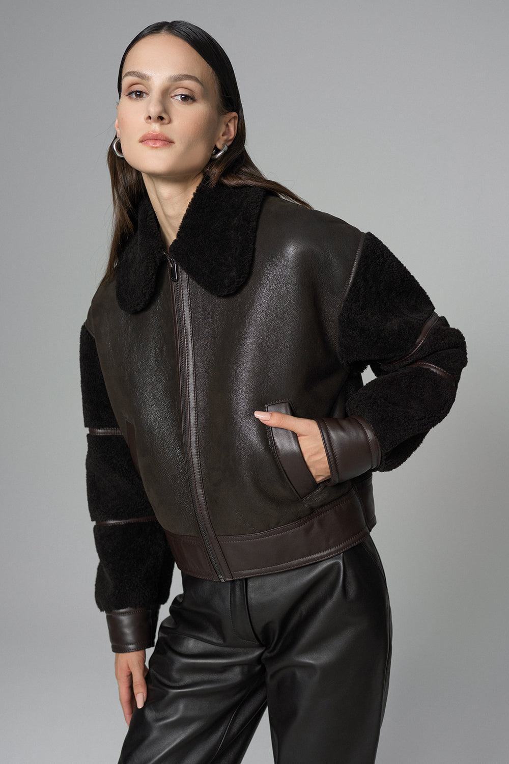 Woman wearing a dark brown leather jacket with fur collar on a gray background