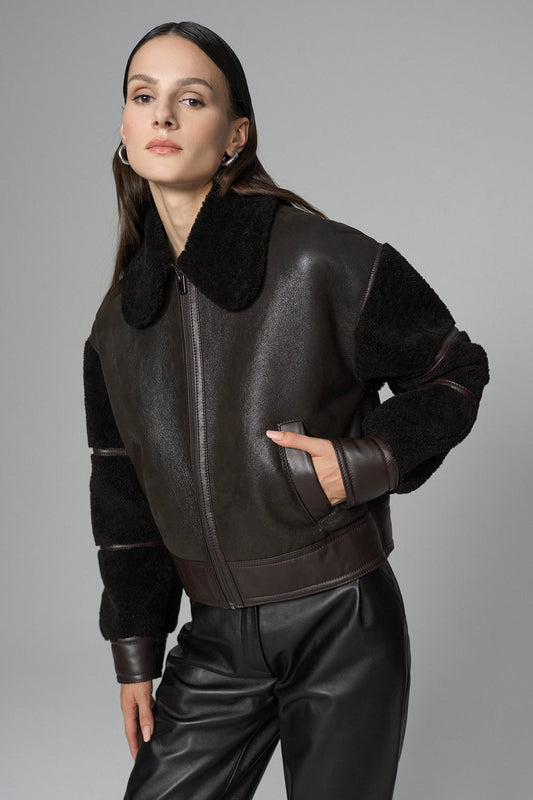 Woman wearing a dark brown leather jacket with fur collar on a gray background