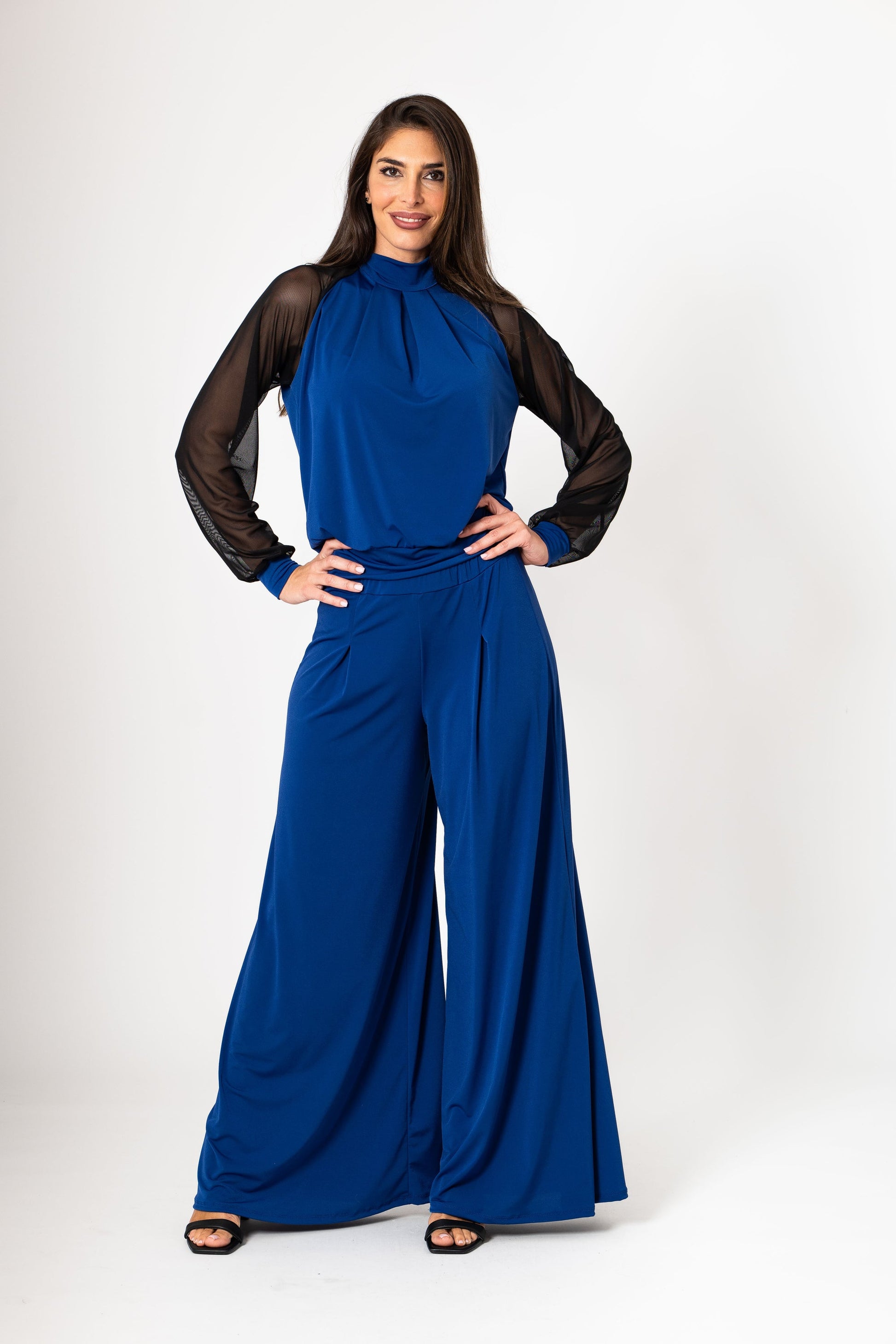 Woman wearing a blue jumpsuit with sheer sleeves on a white background