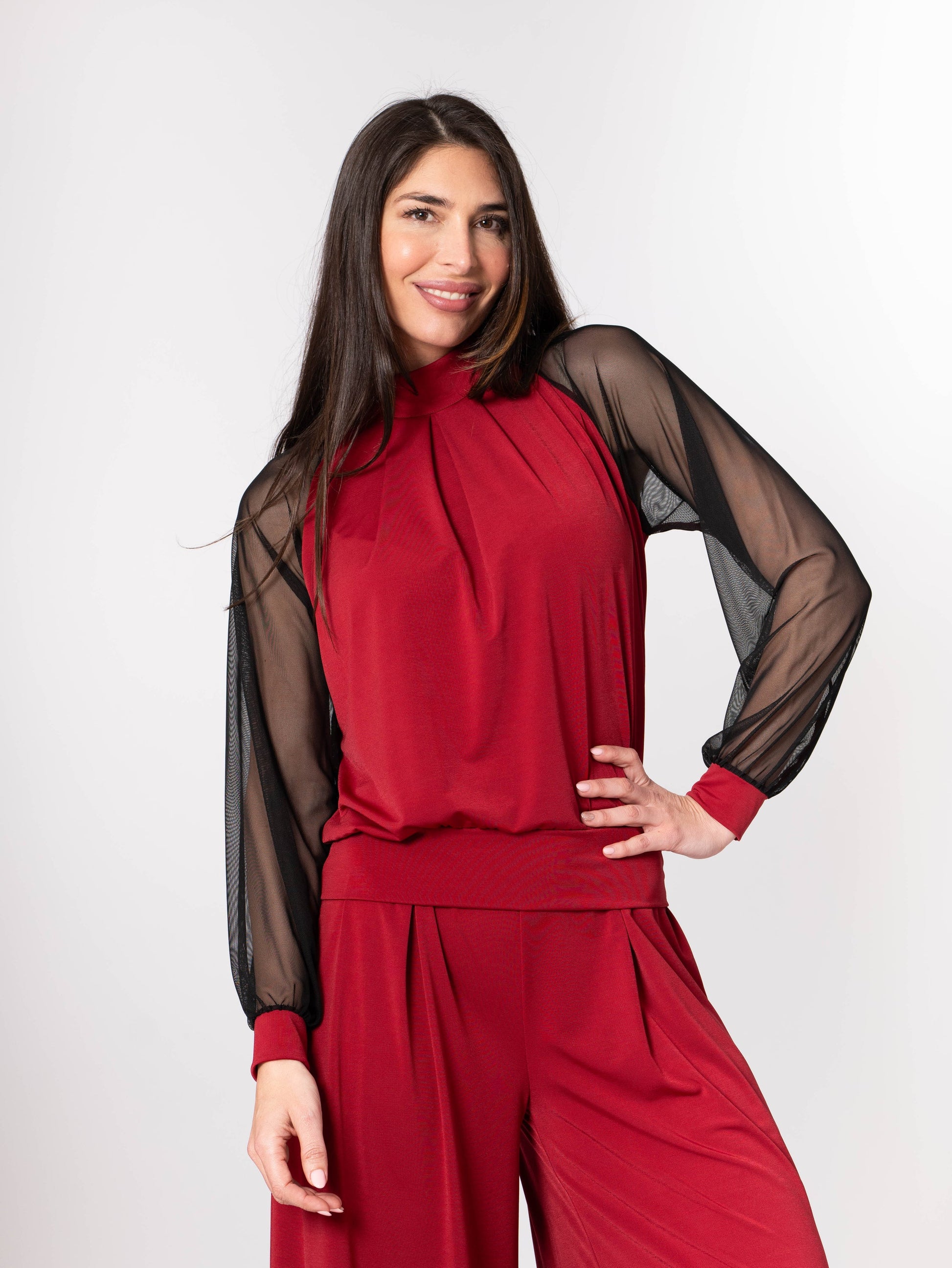 Woman wearing a red outfit with sheer sleeves against a white background