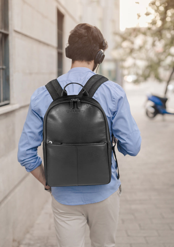 Man wearing a black backpack and headphones, walking on a street.