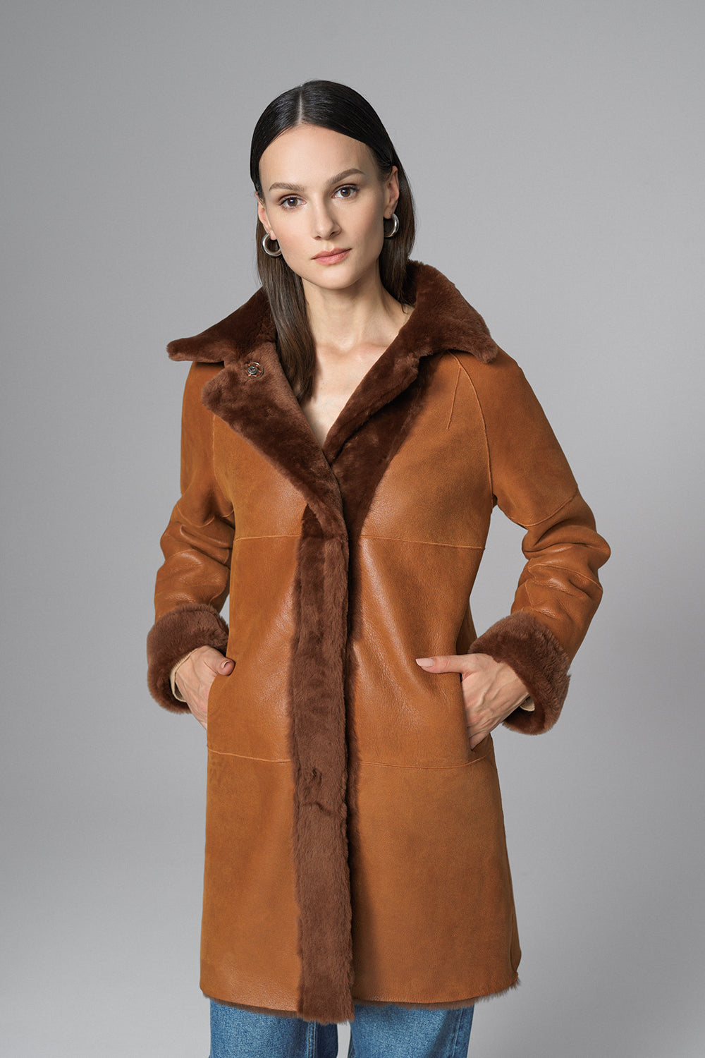 Woman wearing a brown leather coat with fur trim on a gray background