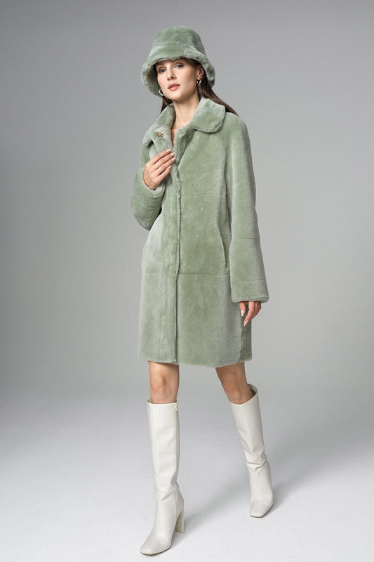 Woman wearing a green coat, hat, and white boots on a gray background