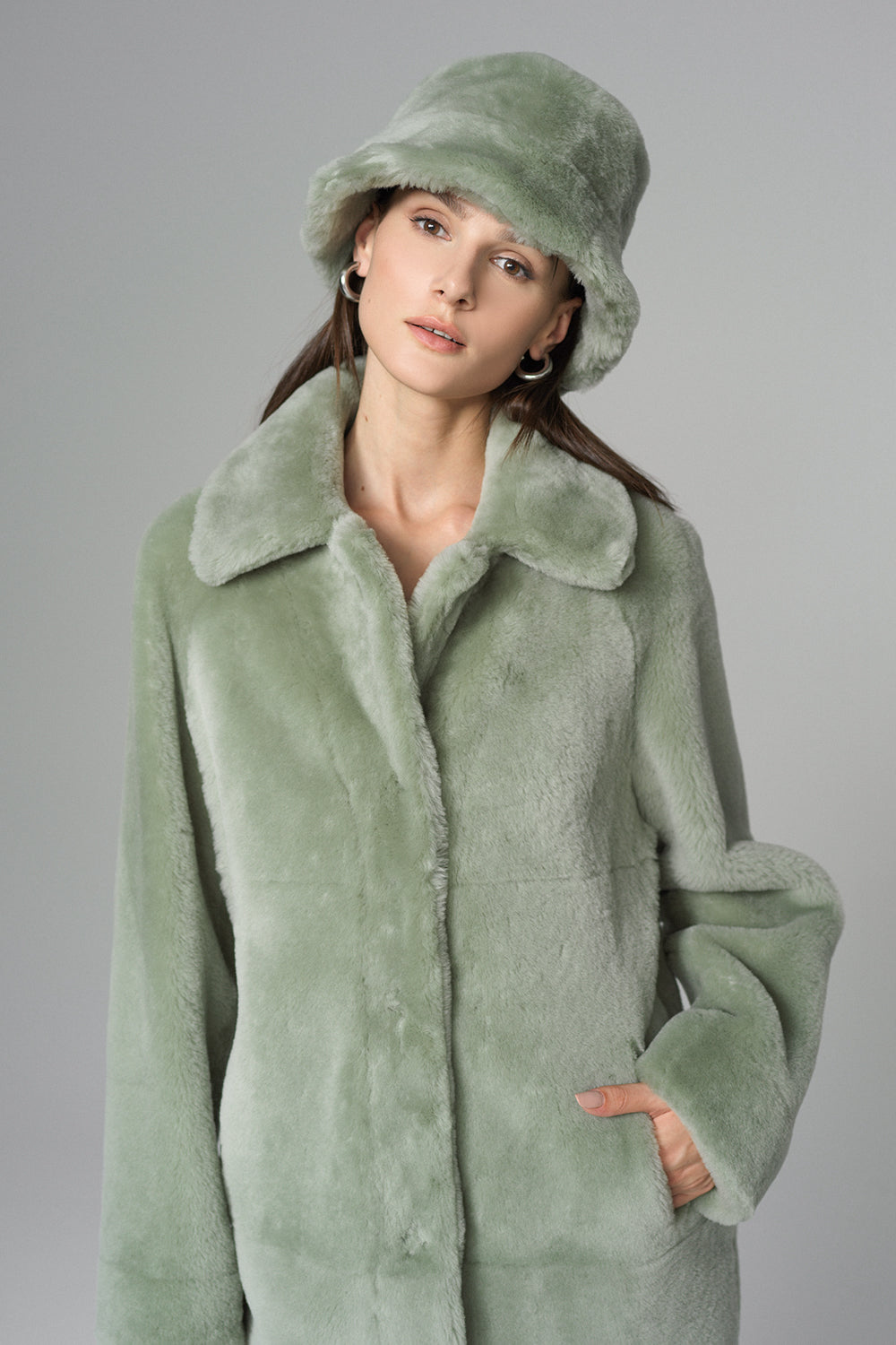 Woman wearing a green coat and matching hat against a gray background