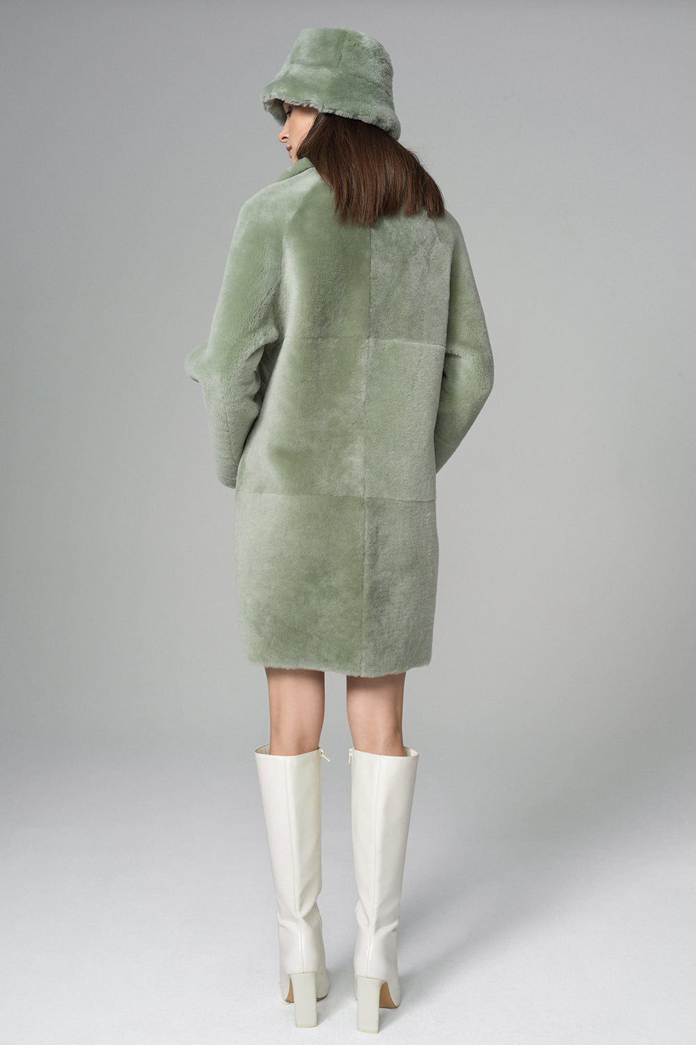 Person wearing a green coat and white boots on a gray background
