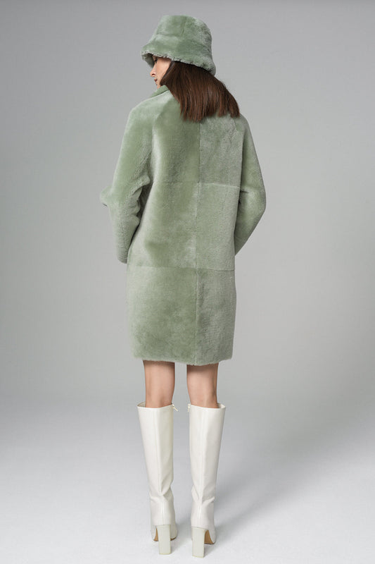 Person wearing a green coat and white boots on a gray background