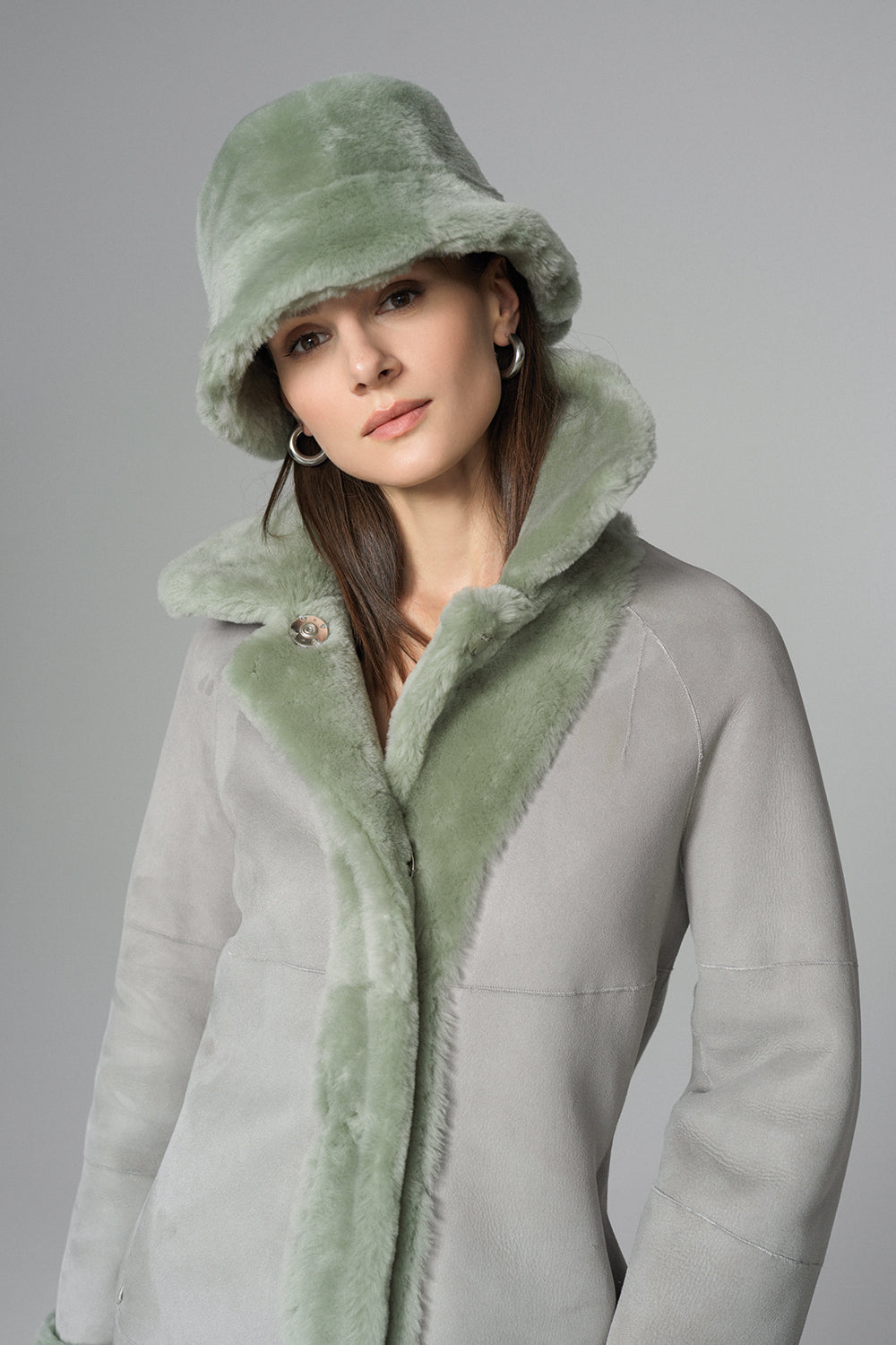 Woman wearing a light gray coat with green fur trim and matching hat