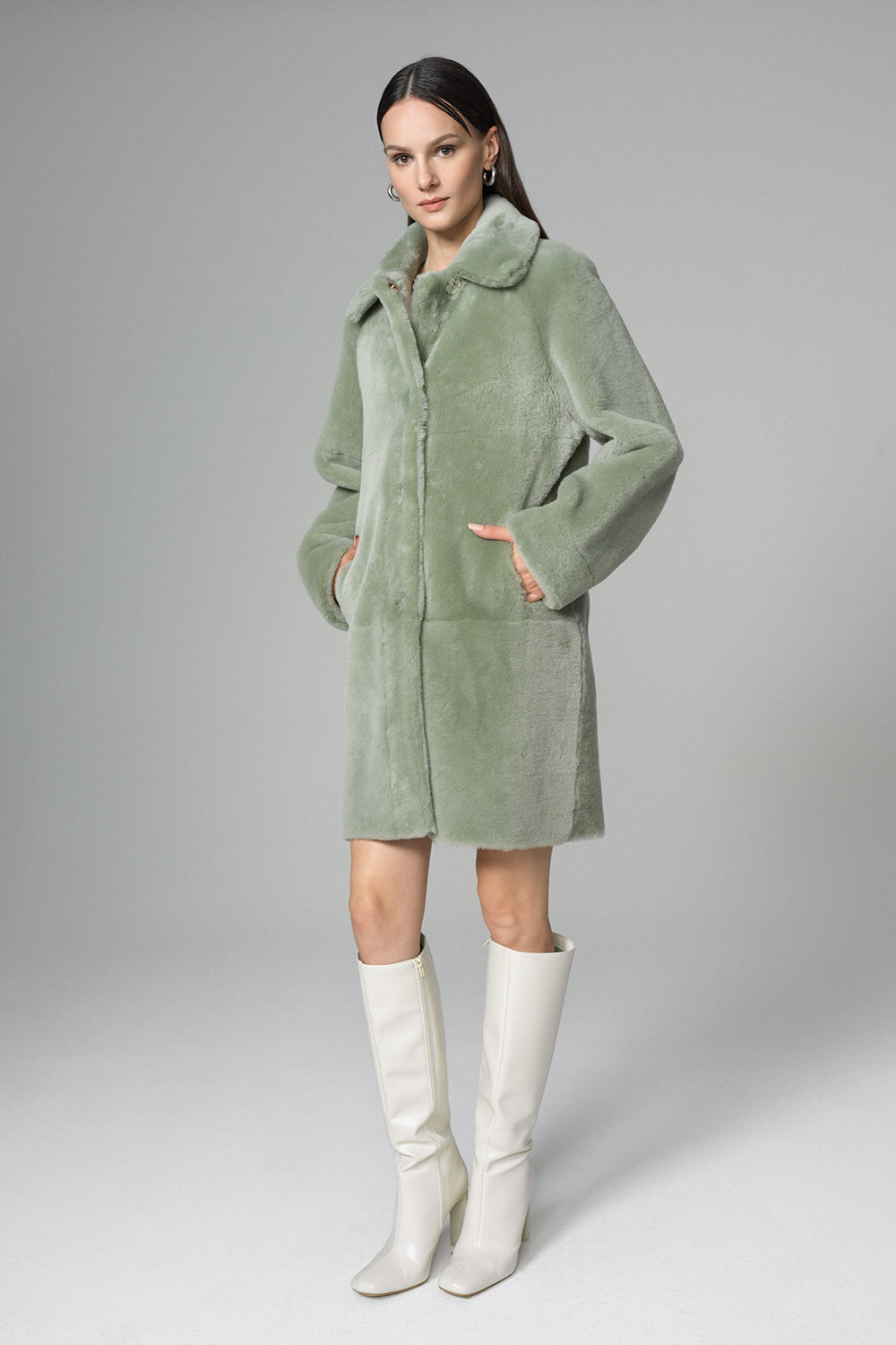 Woman wearing a green coat and white boots on a gray background
