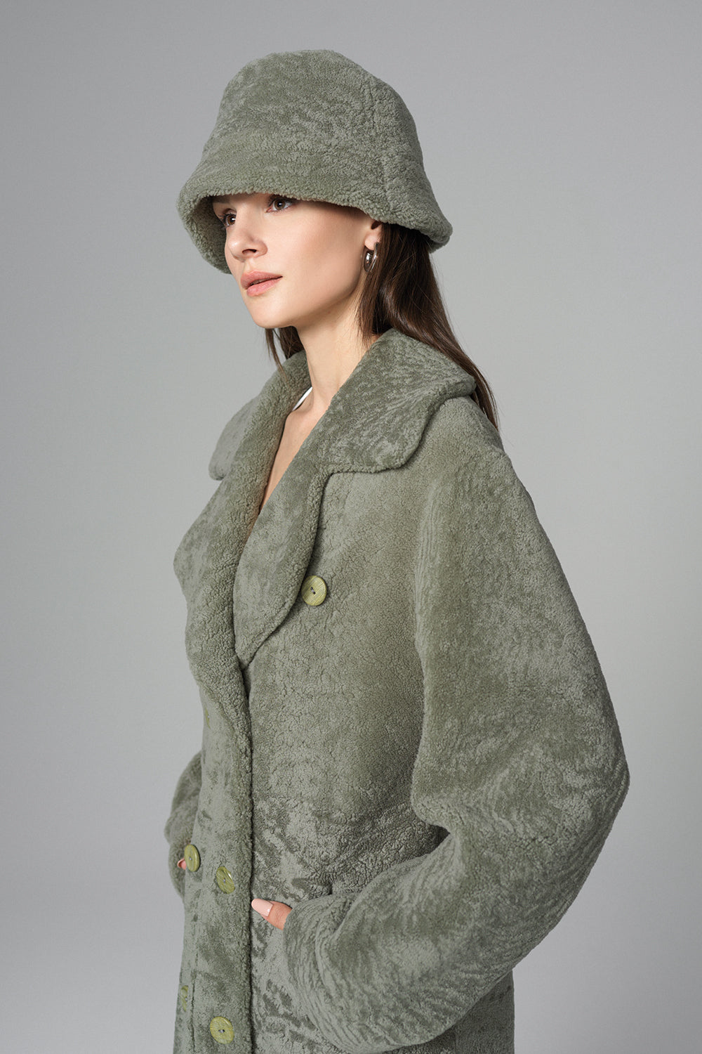 Woman wearing a green coat and matching hat against a gray background