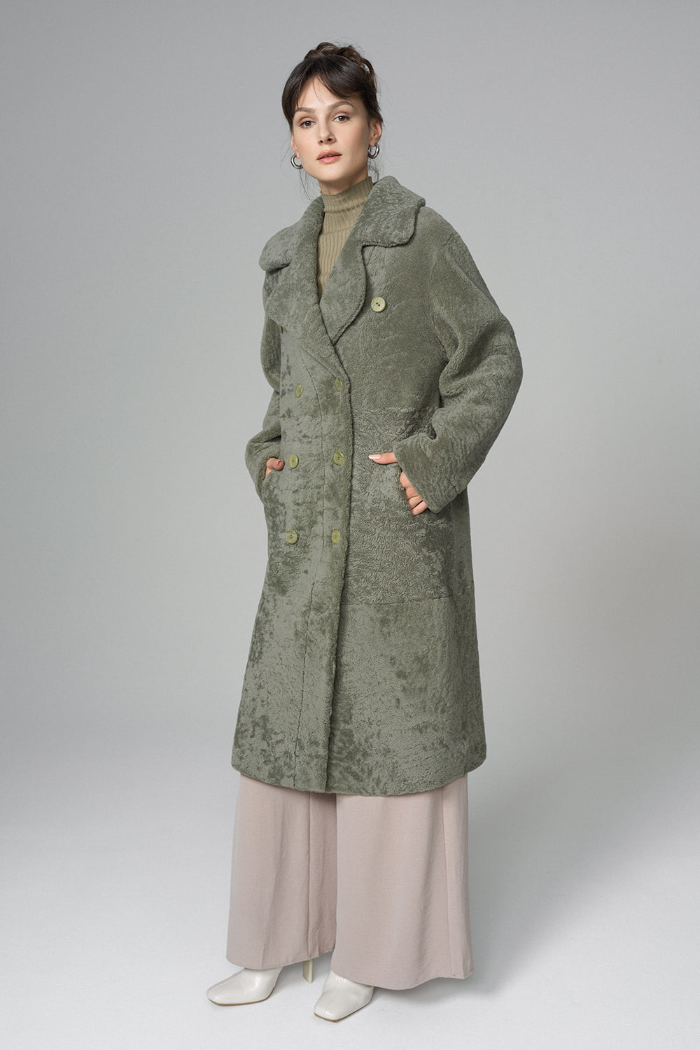 Woman wearing a long green coat on a plain background
