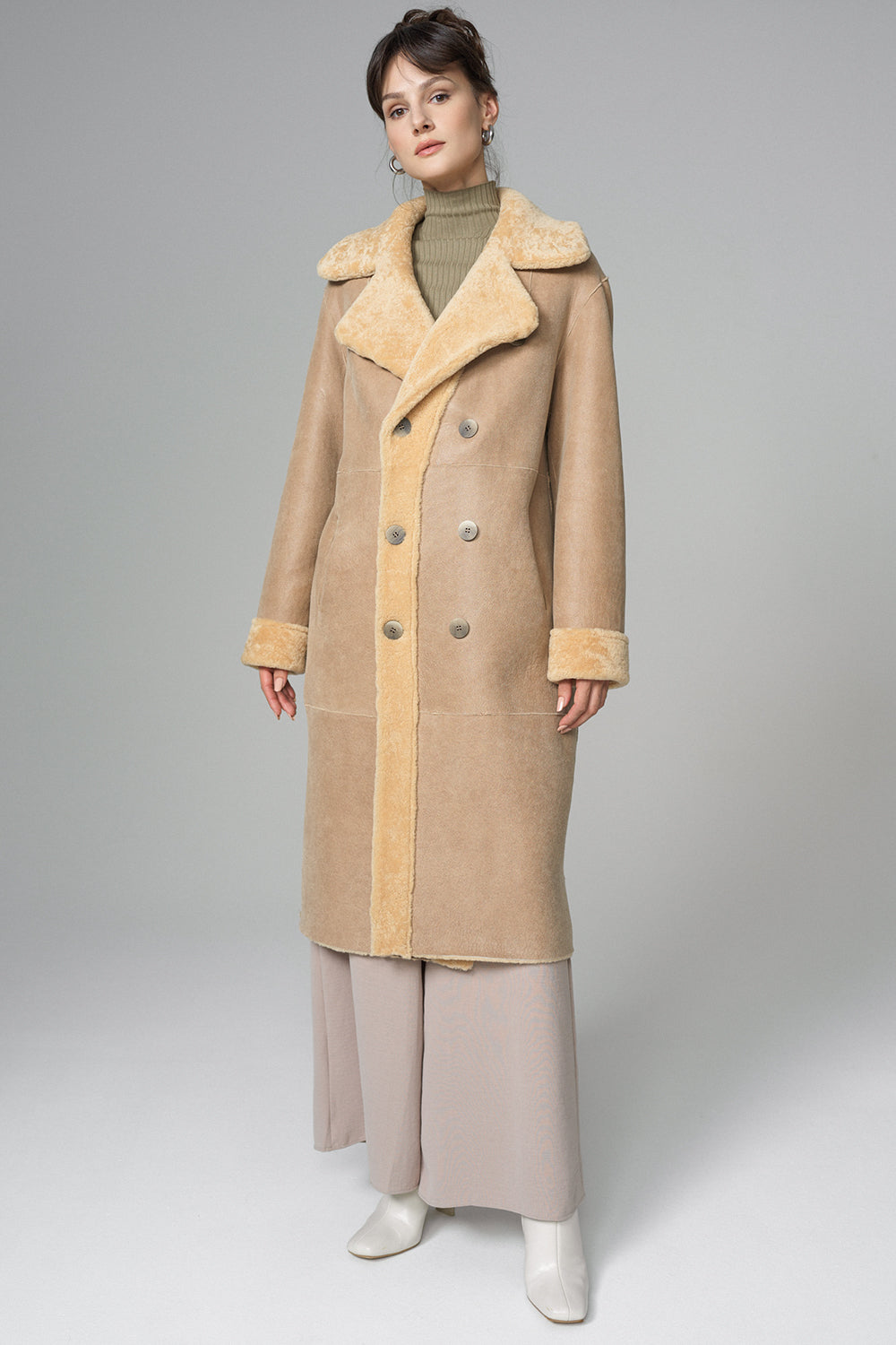 Woman wearing a beige coat with a fur collar on a gray background