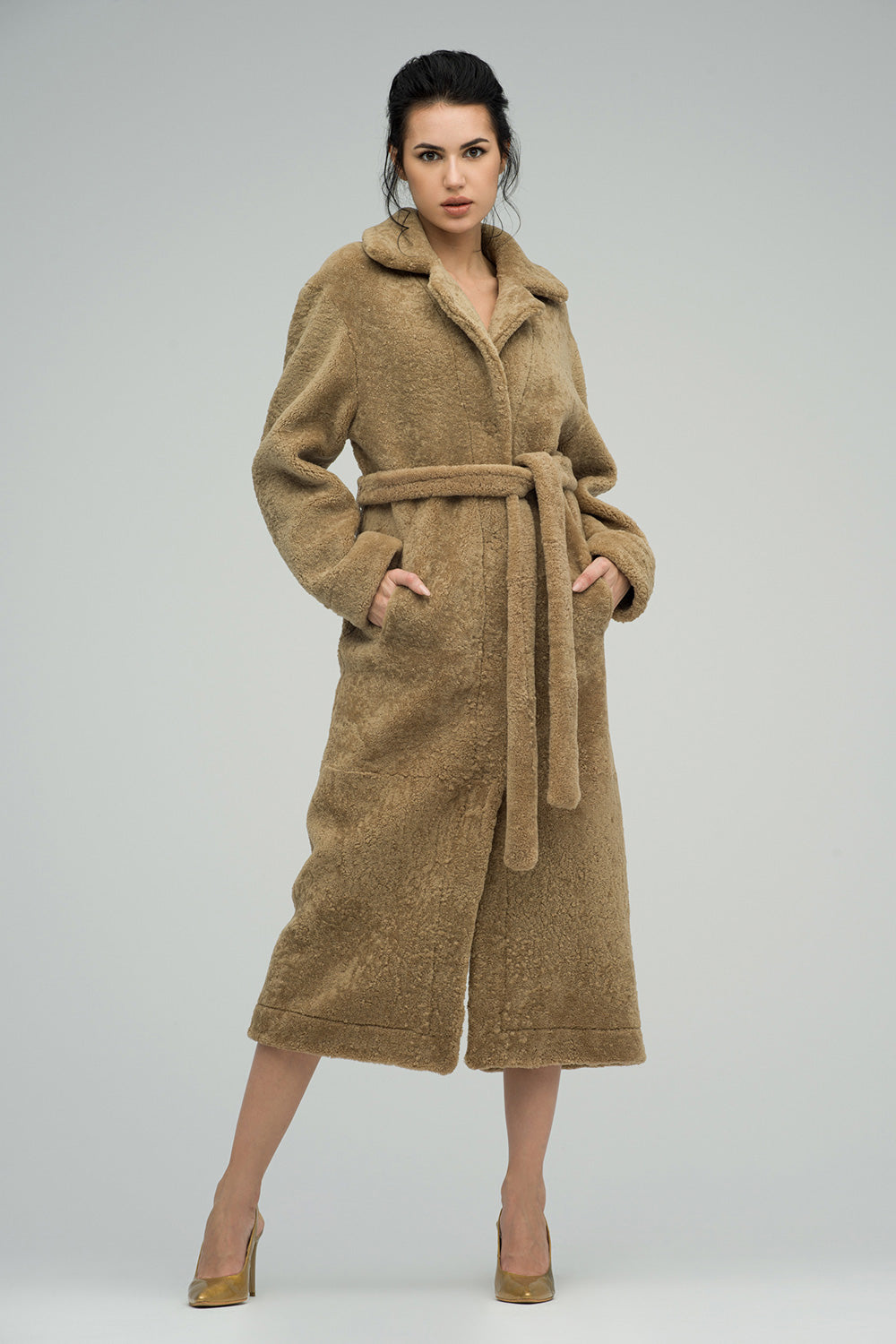 Woman wearing a long beige coat on a plain background