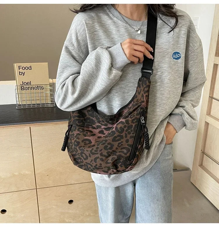 Person wearing a gray sweatshirt and light blue jeans, holding a leopard print bag indoors.