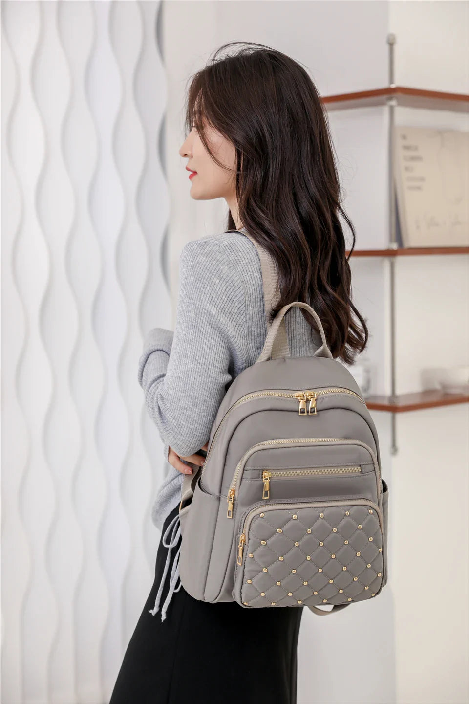 Woman wearing a gray backpack with studded details in an indoor setting