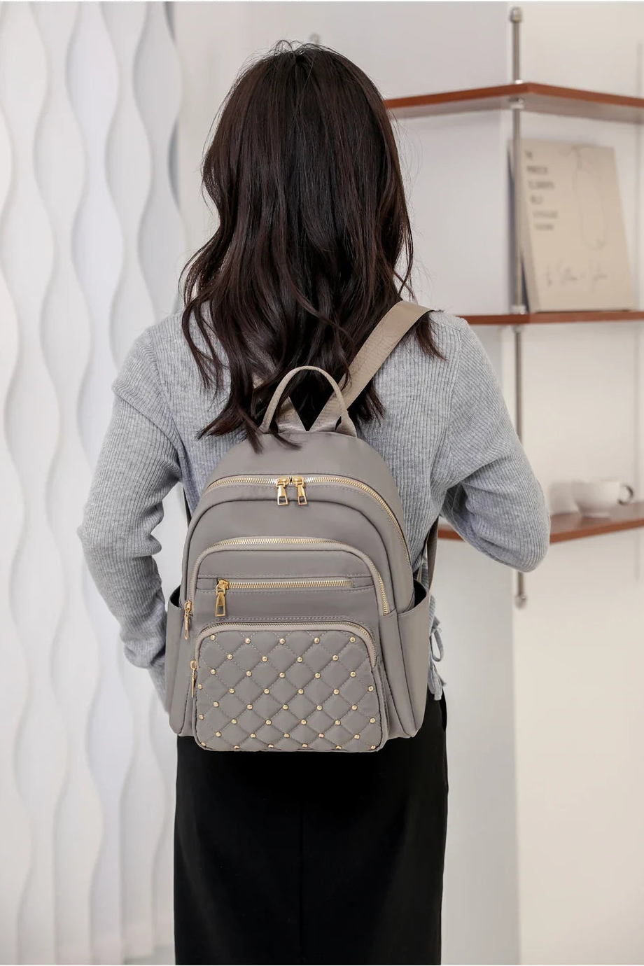 Person wearing a gray quilted backpack indoors