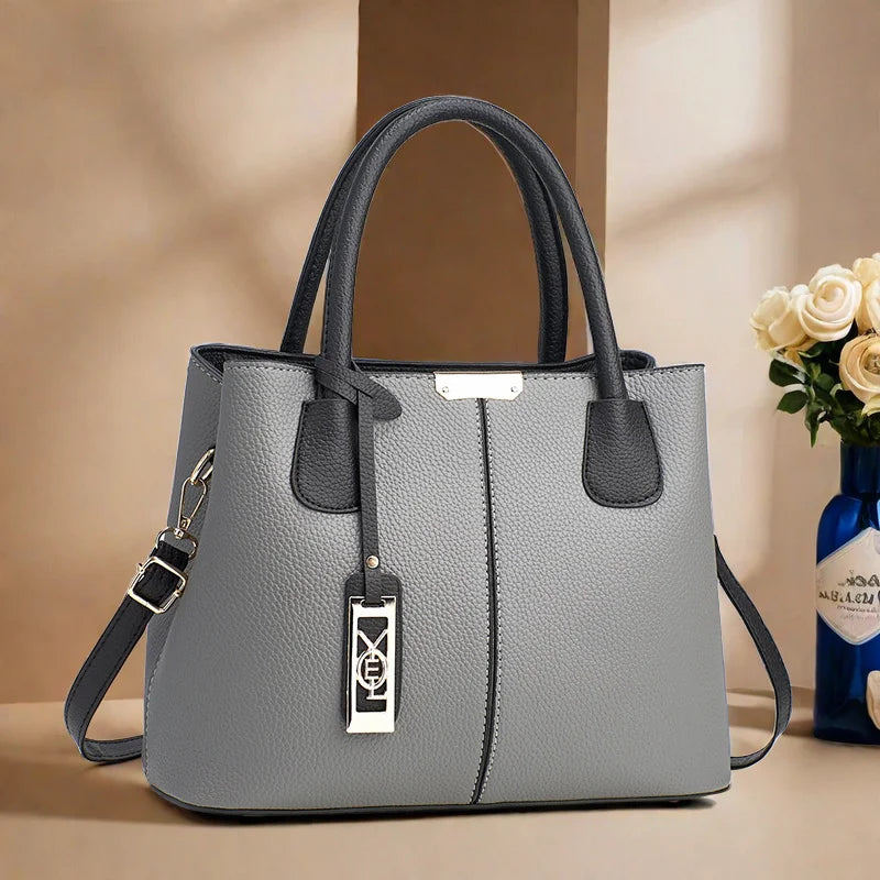 Gray handbag with black accents on a beige surface with a blurred background