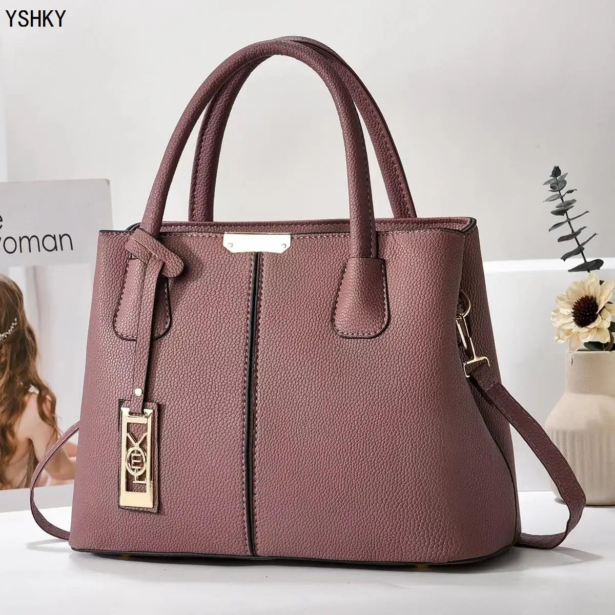 Purple handbag with gold accents on a white surface, with 'YSHKY' branding.