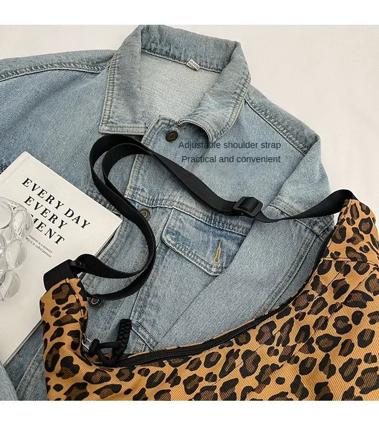 Leopard print bag with black strap over a denim jacket on a light background