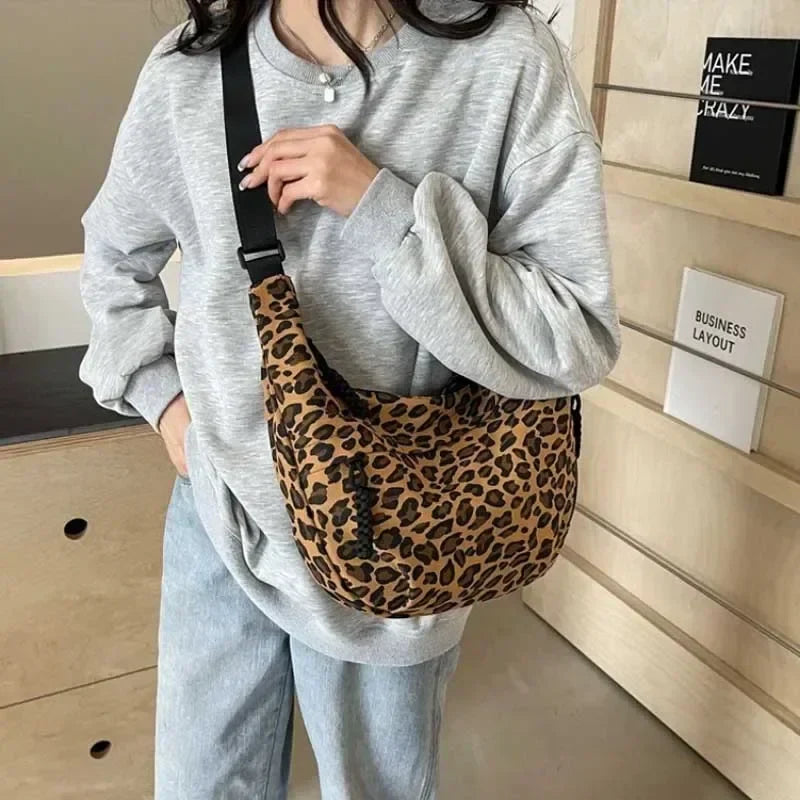 Person wearing a gray sweatshirt and light blue jeans holding a leopard print bag.