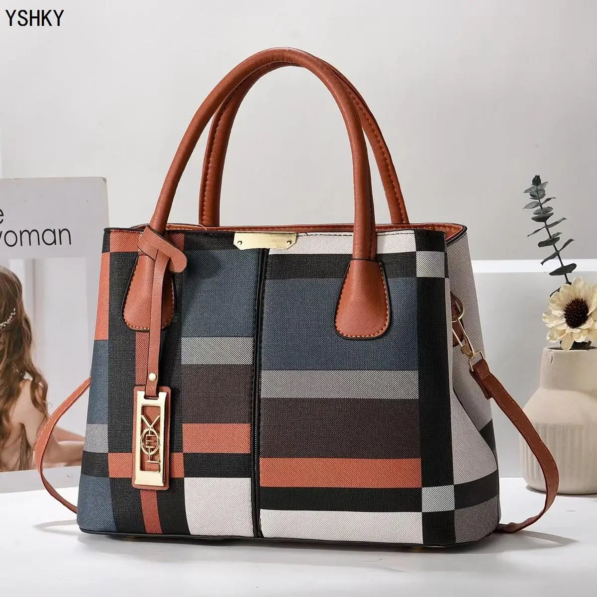 Multicolored checkered handbag with brown handles and strap on a white surface.