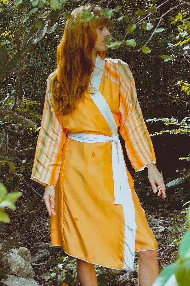 Woman in an orange dress with a white belt standing in a forest setting