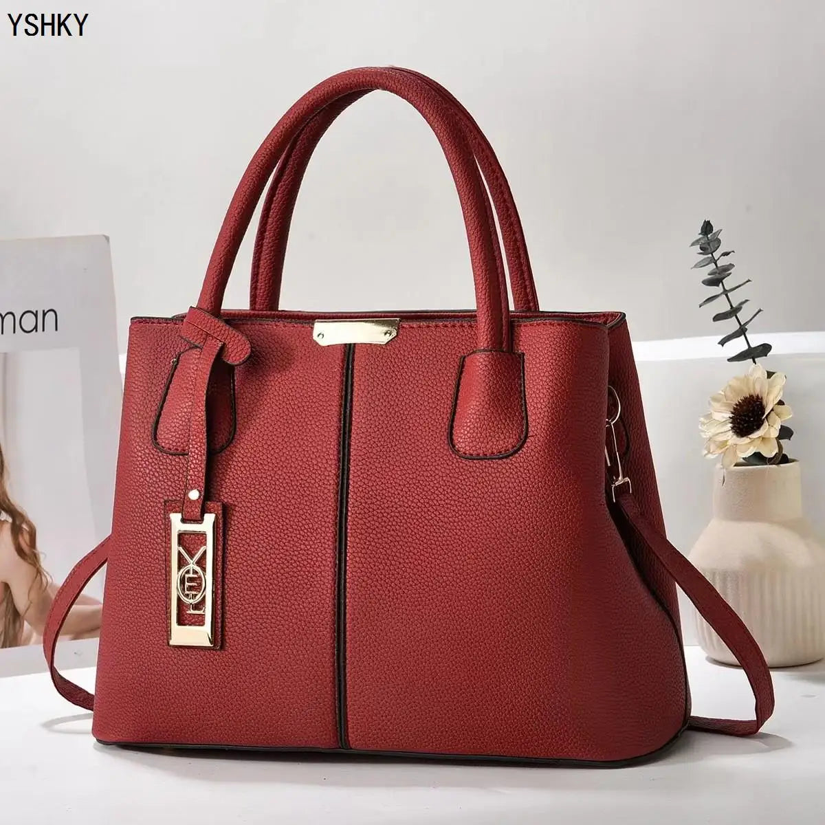 Red handbag with gold accents on a white surface, branded 'YSHKY'.