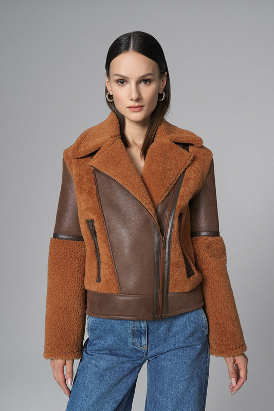 Woman wearing a brown shearling jacket with leather panels on a gray background