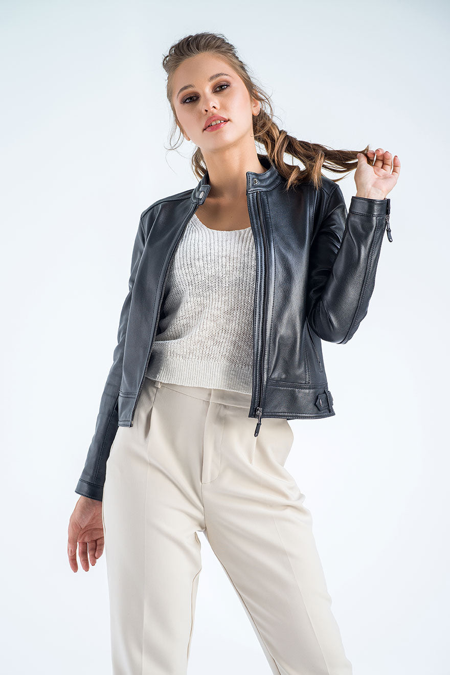 Woman wearing a black leather jacket over a white sweater and beige pants on a light gray background
