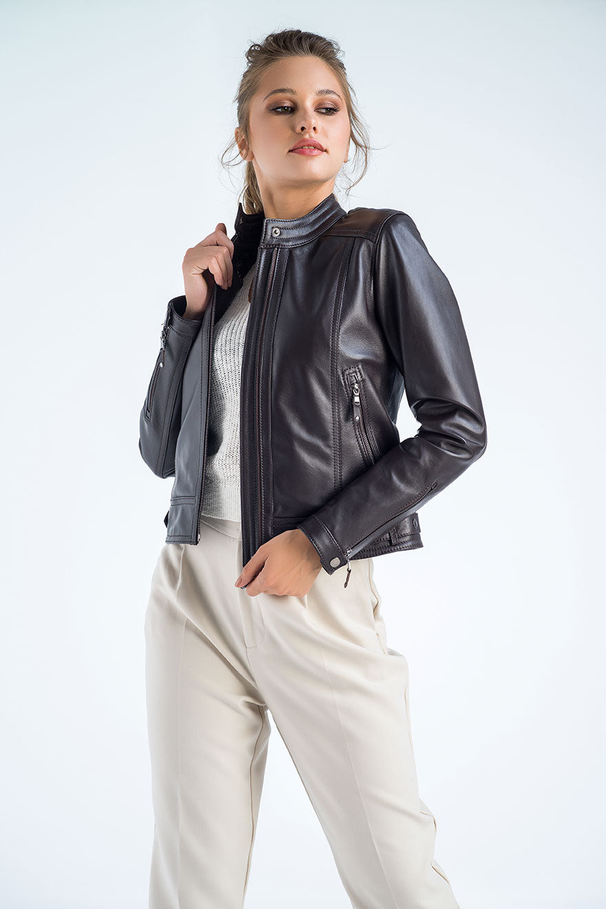 Woman wearing a brown leather jacket over a white top and beige pants on a light gray background