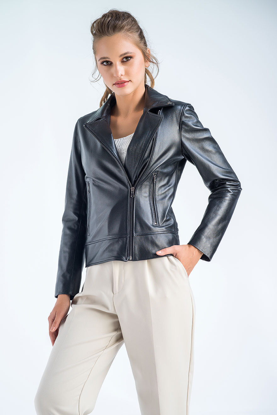 Woman wearing a black leather jacket and white pants on a light gray background