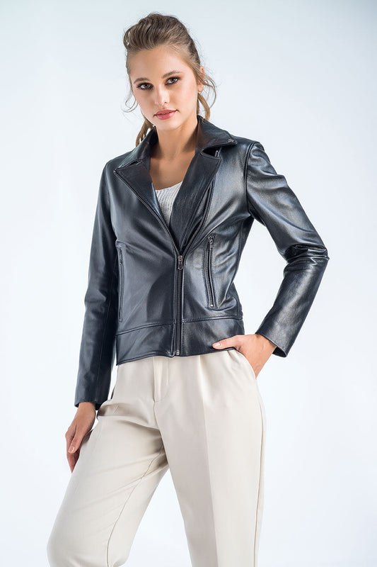 Woman wearing a black leather jacket and white pants on a light gray background