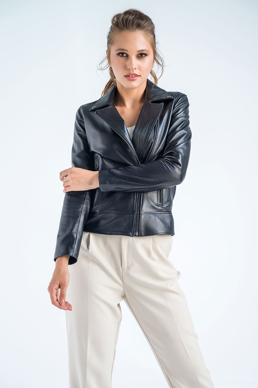 Woman wearing a black leather jacket and white pants on a light gray background