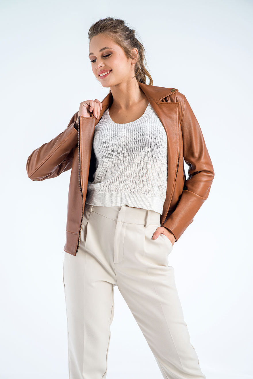 Woman wearing a brown leather jacket, white sweater, and beige pants on a white background