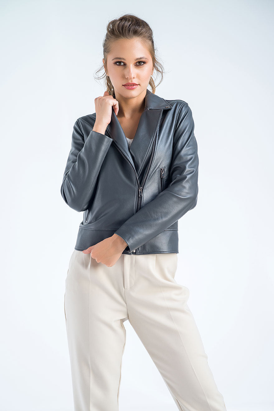 Woman wearing a gray leather jacket and white pants on a light gray background