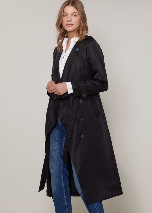 Woman wearing a black coat over a white shirt and blue jeans on a plain background