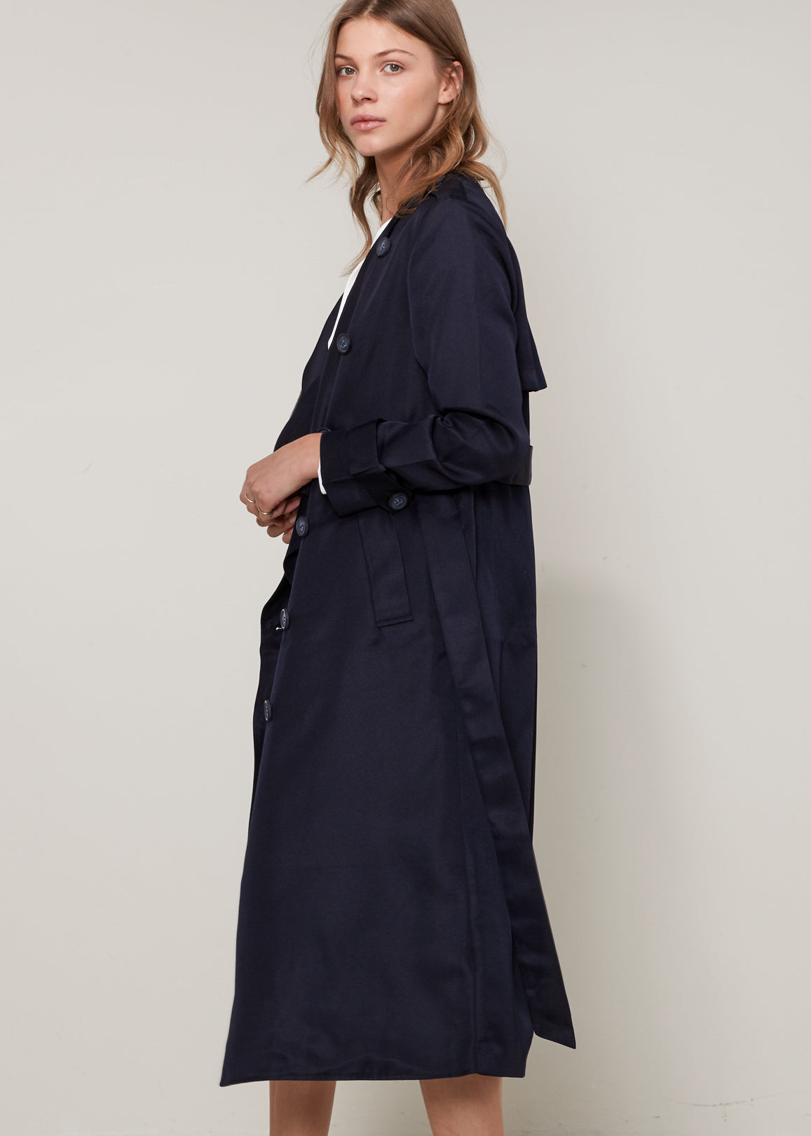 Woman wearing a navy trench coat against a plain background