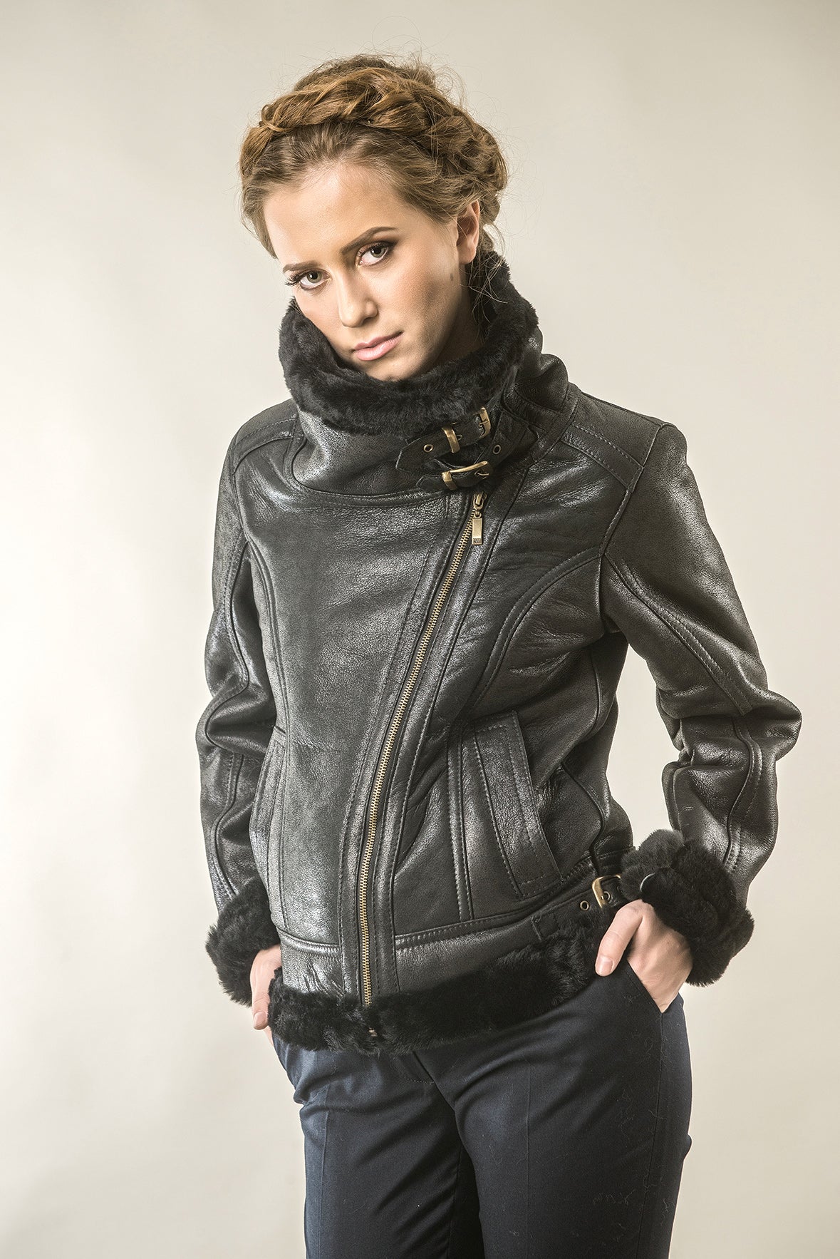 Woman wearing a black leather jacket with fur trim on a plain background