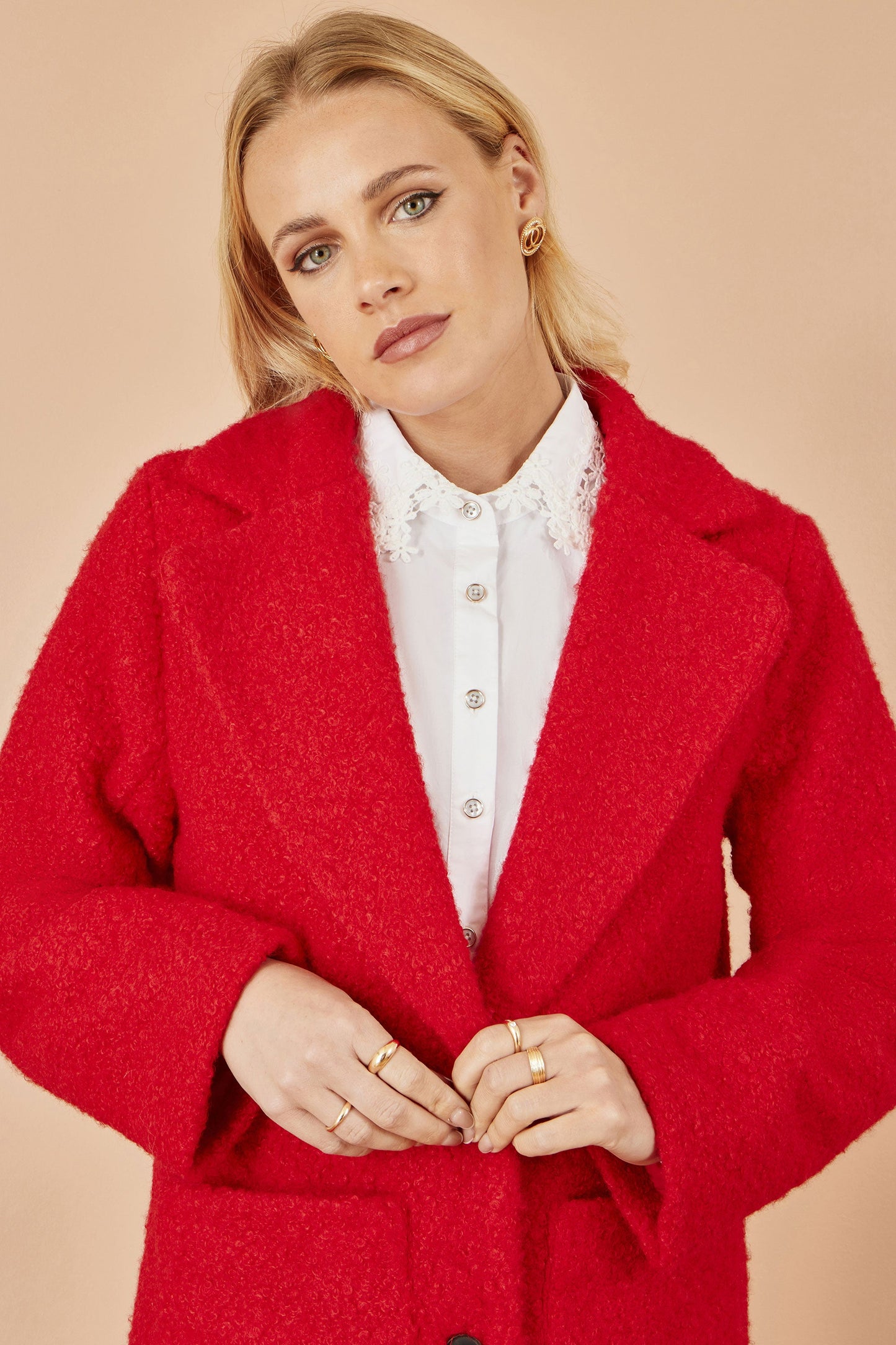 Woman wearing a red coat over a white shirt on a beige background