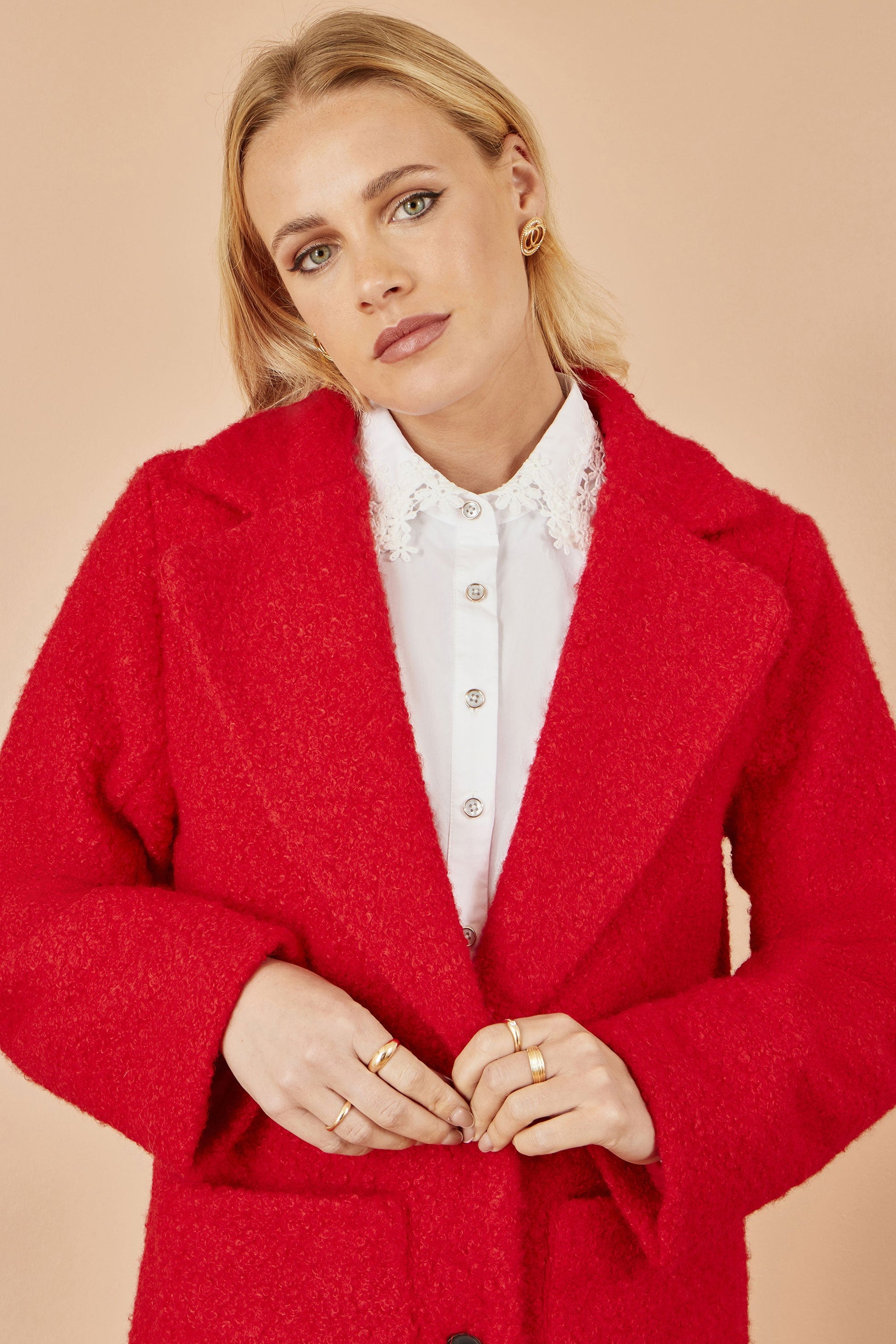 Woman wearing a red coat over a white shirt on a beige background