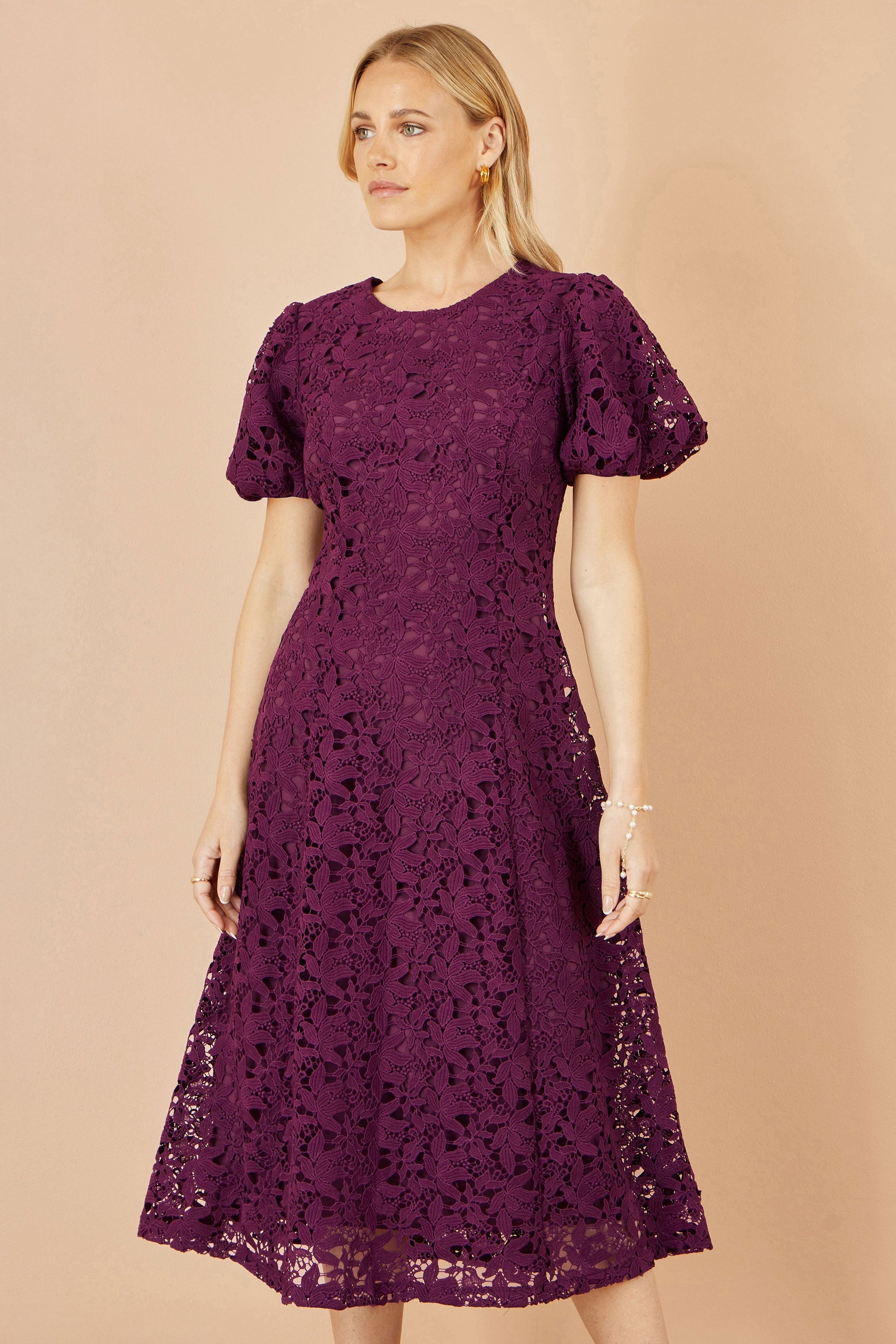 Woman wearing a purple lace dress against a beige background